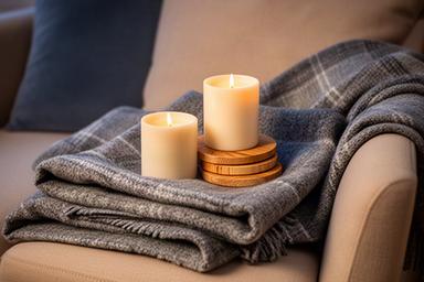 Cadeauset met wollen plaid, twee kaarsen en houten onderzetters op een fauteuil