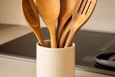 Set houten keukenhulpen in een keramieken pot naast een kookplaat