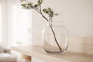 Transparante glazen vaas met enkele tak op een lichte houten plank