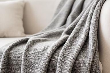 Grijze plaid met grove textuur over een lichte bank